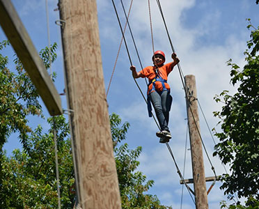 A kid walks across a sky-high tight rope in a park