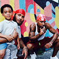 A bow and two men pose for a family portrait against a mural in a park