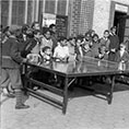 archival black and white photo of kids playing ping pong outdoors at Marcus Garvey Park as a crowd of other kids look on