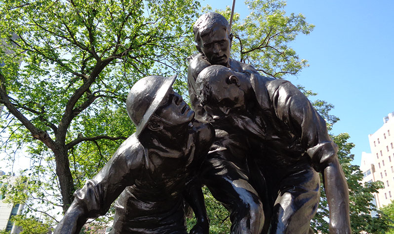 The statue depicts two soldiers, one kneeling and one standing, supporting a third slumping comrade in battle.