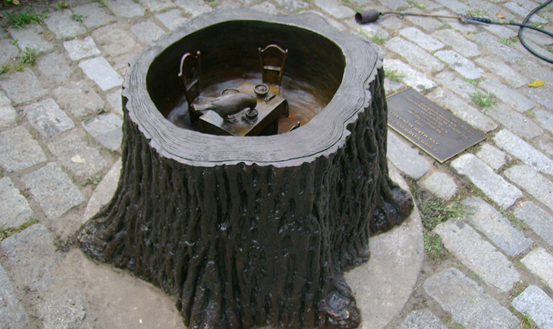 A miniature vignette, in which a bird has happened upon the remains of a meal at a tiny table setting, is contained within the stump of a tree.