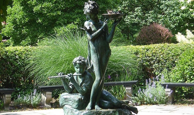 Surrounded by the park's greenery and benches, the Burnett Memorial, which also includes a fountain, depicts in bronze a standing girl holding a bowl, a boy playing a flute reclining beside her, and swallows.