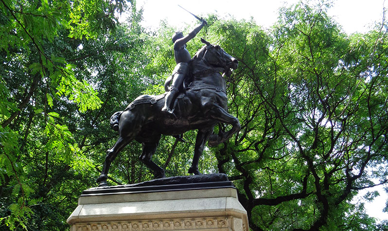 The statue, on a pedestal, depicts Joan of Arc riding a horse with a sword in hand and pointed in the air.