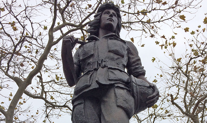 A bronze statue of a woman in uniform and holding a helment.