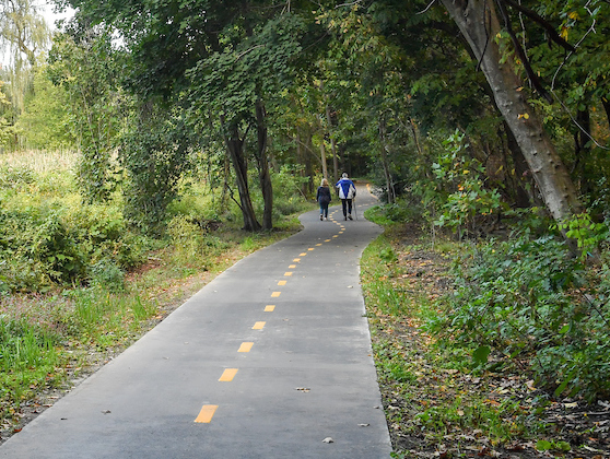 a guest with a walking cane walks with a companion on a paved, accessible trail through the park