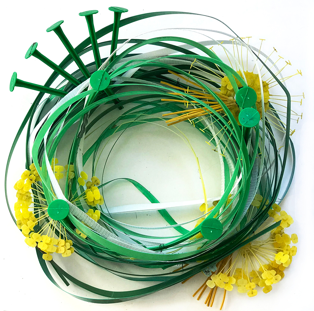 Green strapping tape form the base of the wreath decorated with yellow twist ties that form a floral pattern and green nails added to the crown of the wreath