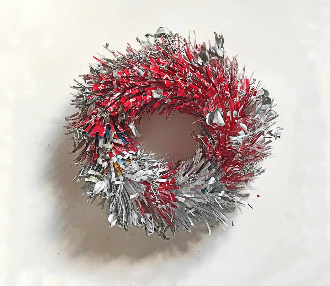 Red and silver diet coke cans are stripped and arranged with bayberry branches to form a wreath