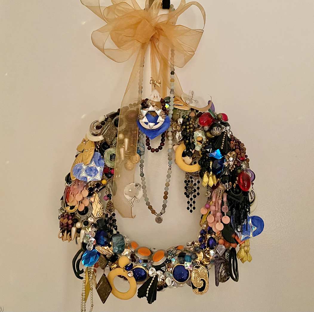 Colorful jewelry in various shapes and sizes, beads, and the Star of David are arranged to form a wreath which hangs from a big gold ribbon