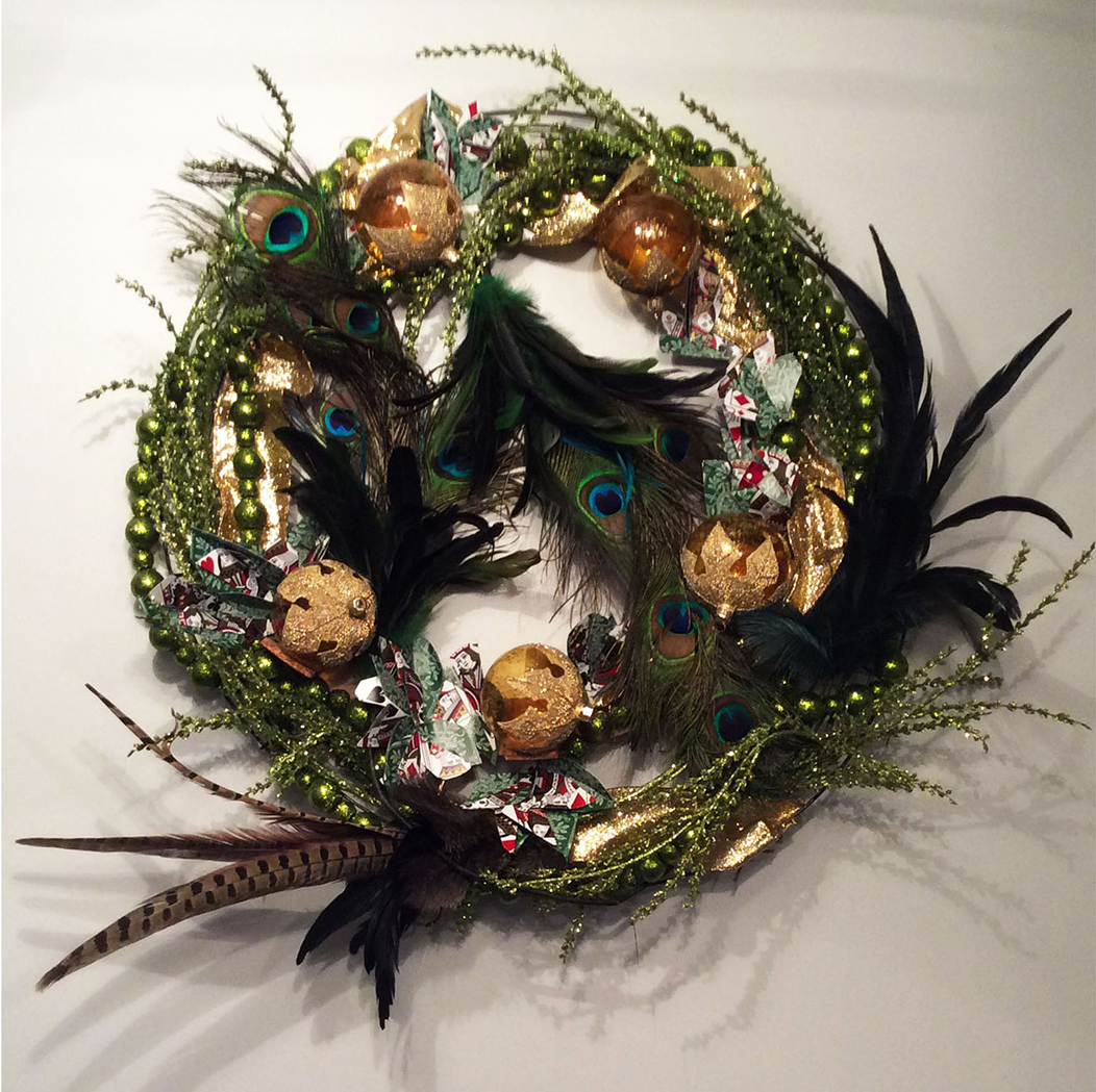 Peacock feathers, beads, playing cards, and light bulbs painted gold are arranged to form a wreath