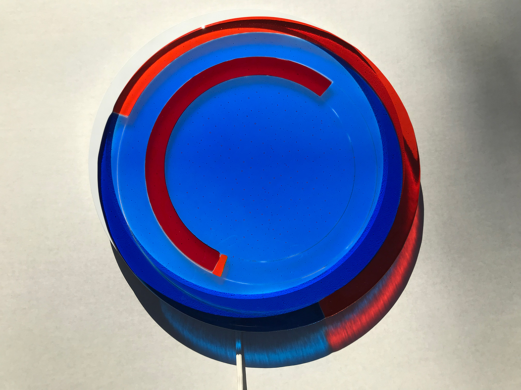 Kiln fused glass in blue and red colors are overlaid on a circular LED flat panel light fixture