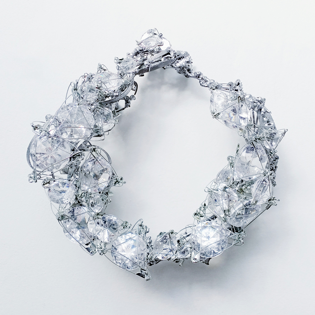 Giant acrylic diamonds are wrapped in the wires of safety pins and placed on a steel base form a wreath