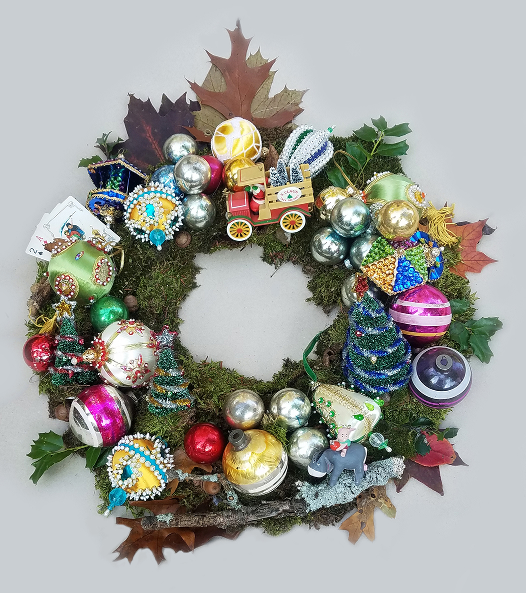 Vintage holiday ornaments including balls and toy trucks are arranged among twigs, leaves, and plants to form a wreath