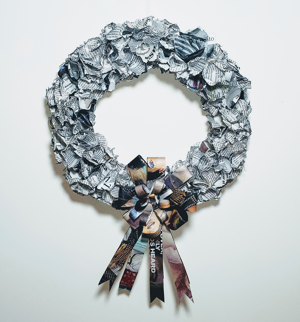 Ripped pieces of newspaper are arranged to form a wreath with the colorful print used to form a bow