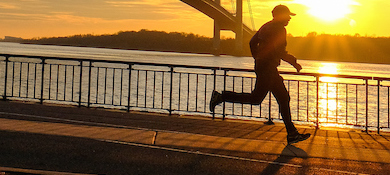 a jogger runs by a waterfront view featuring the bridge and sunset