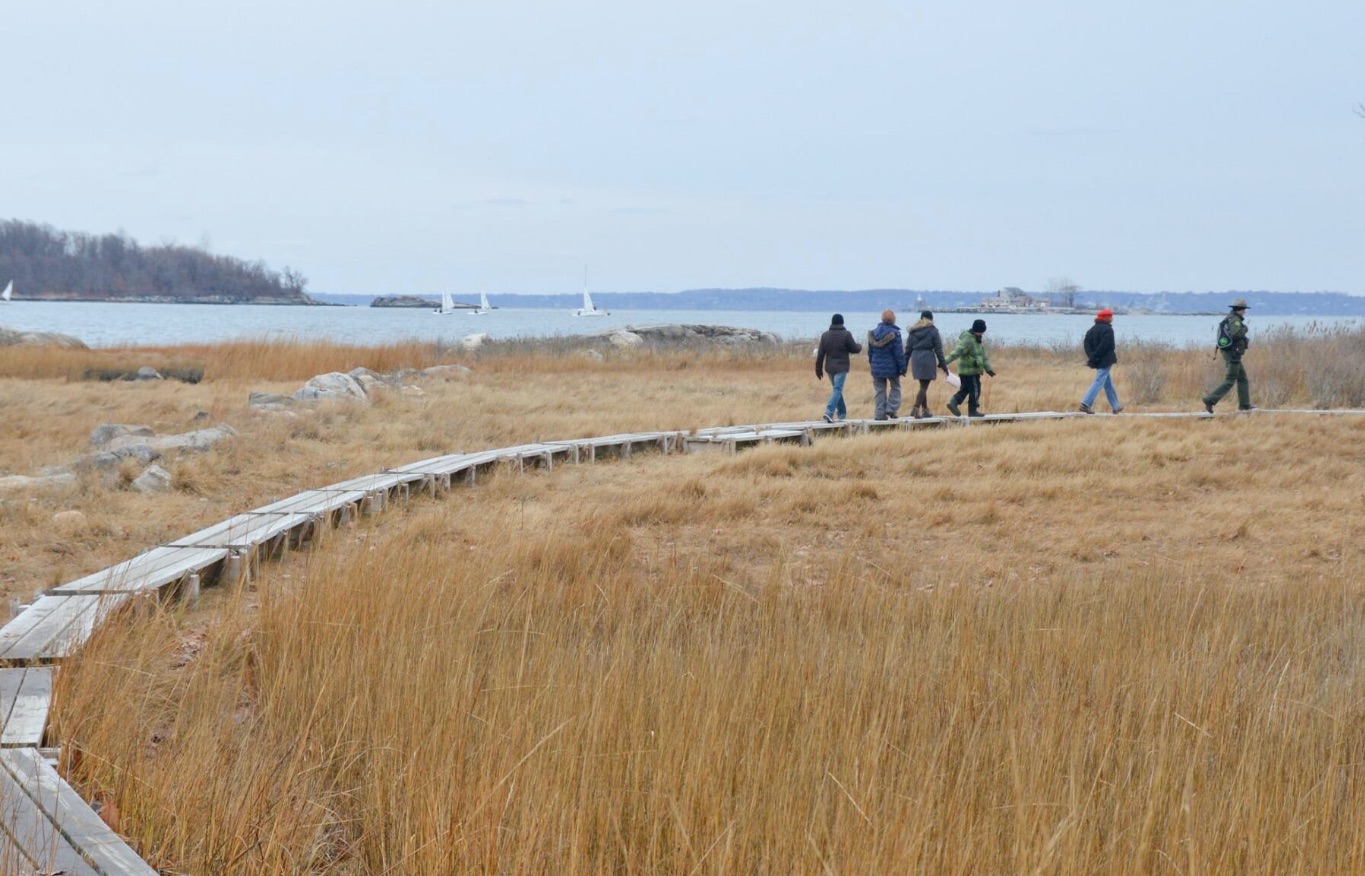 a park ranger leads hikers on a wooden trail that winds through a meadow by the waterfront