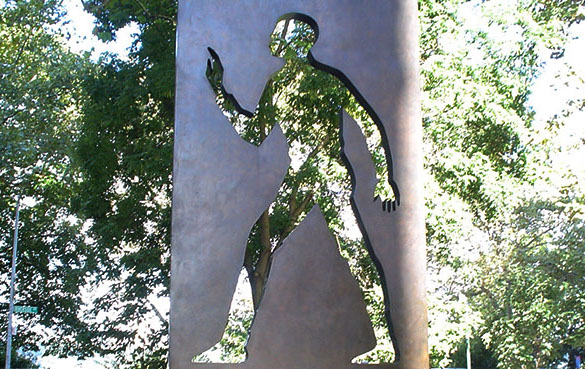 statue of a figure of a man carved out from a bronze monolith against the backdrop of a park