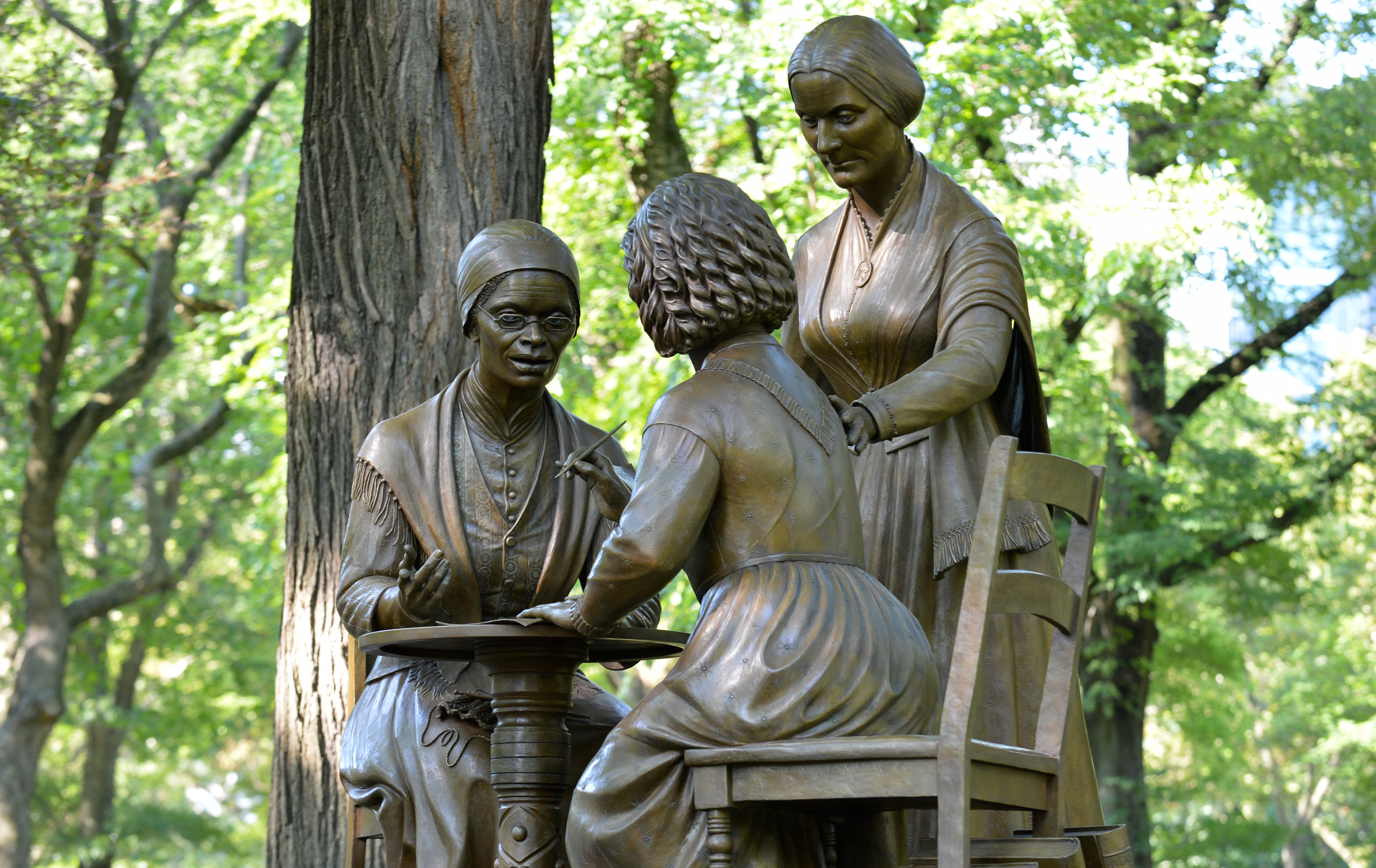 Bronze monument of Sojourner Truth talking at a table where Susan B. Anthony is standing and organizing and Elizabeth Cady Stanton is writing