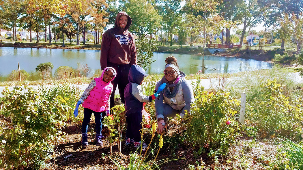 A family tends to plants near a pond in the park