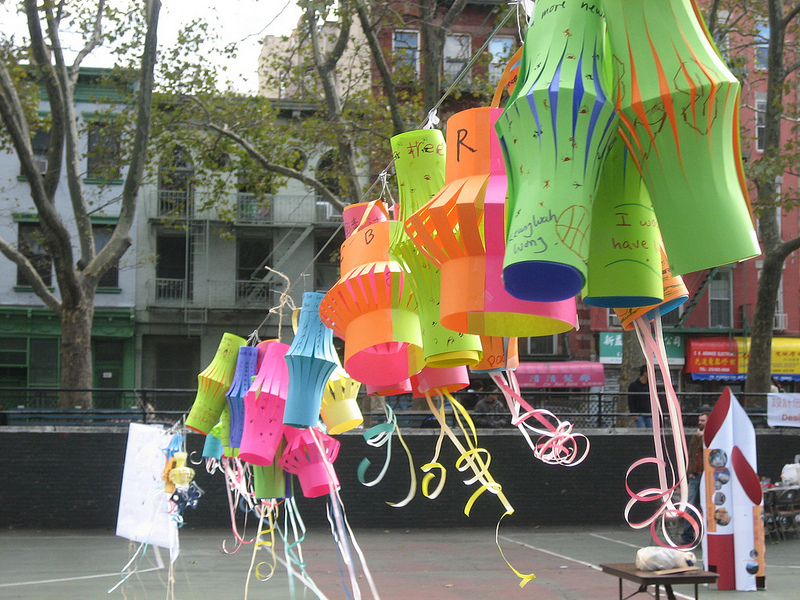 Paper wish lanterns in various colors hang from a clothes line in a park