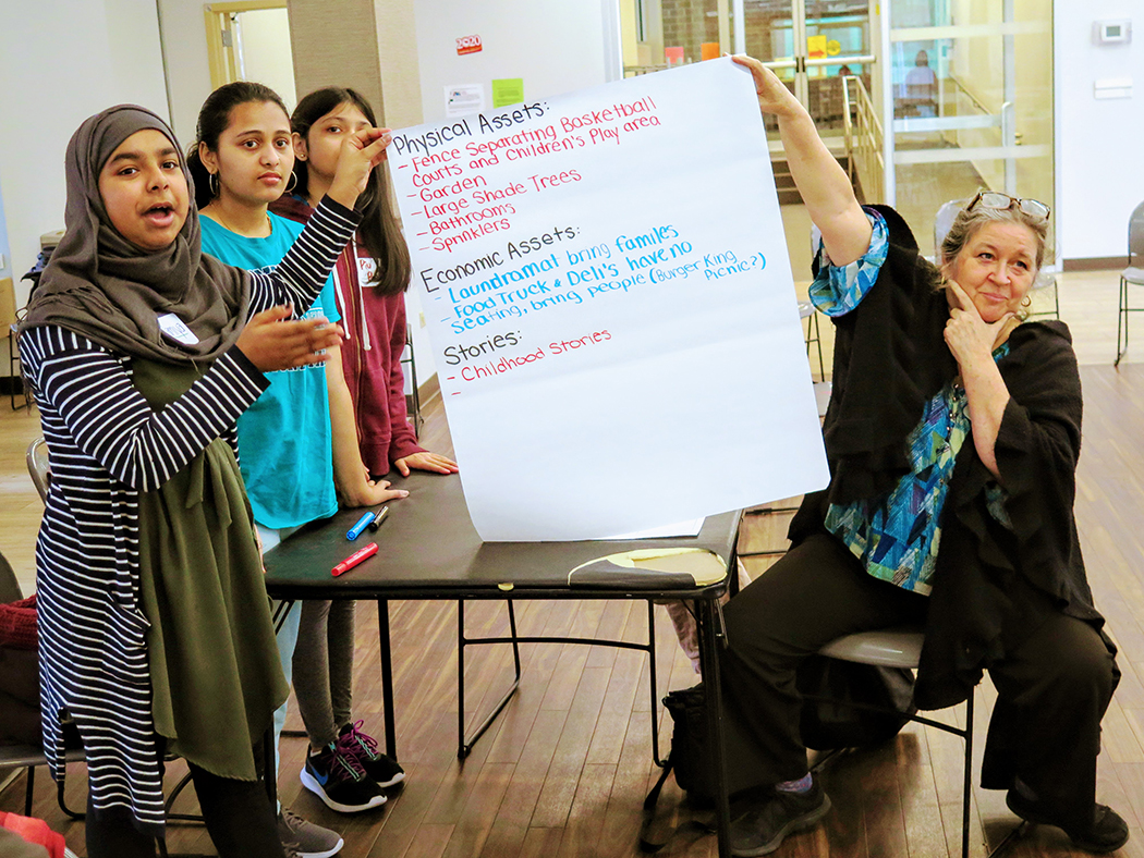 Kids help hold up a giant list that addresses physical assets, economic assets, and stories about their neighborhood and park