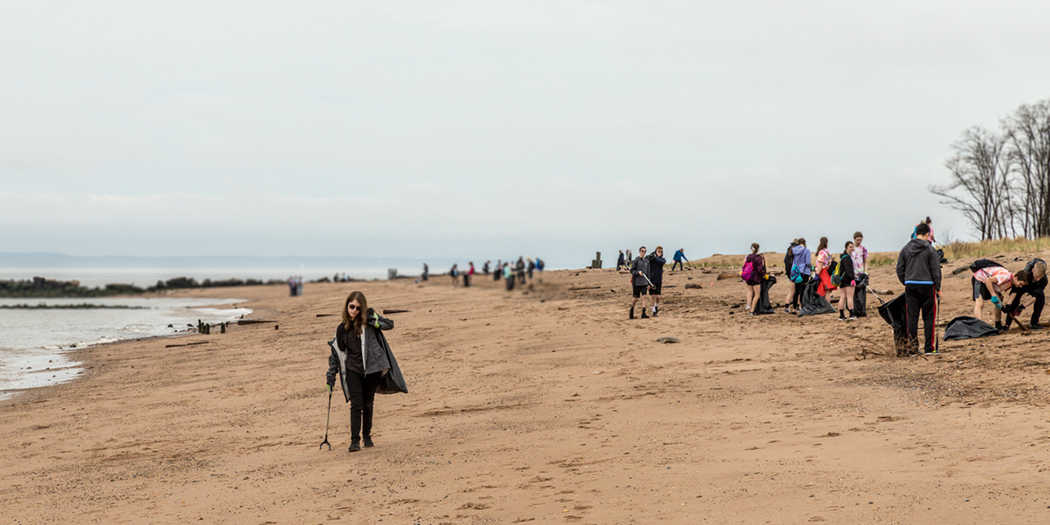 community members use grabbing sticks to pick up trash along a beach