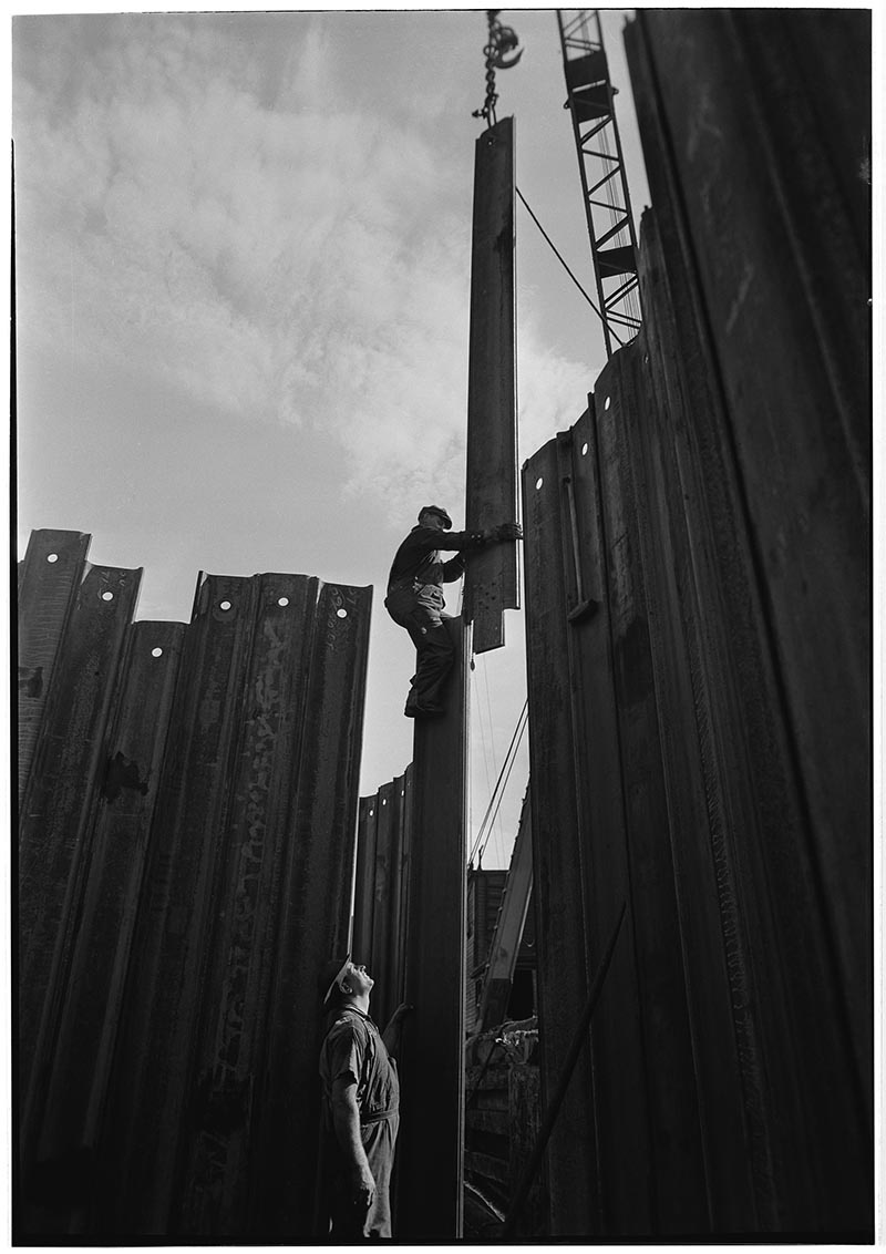 black and white archival image of a worker puts together a wall of steel at the construction site