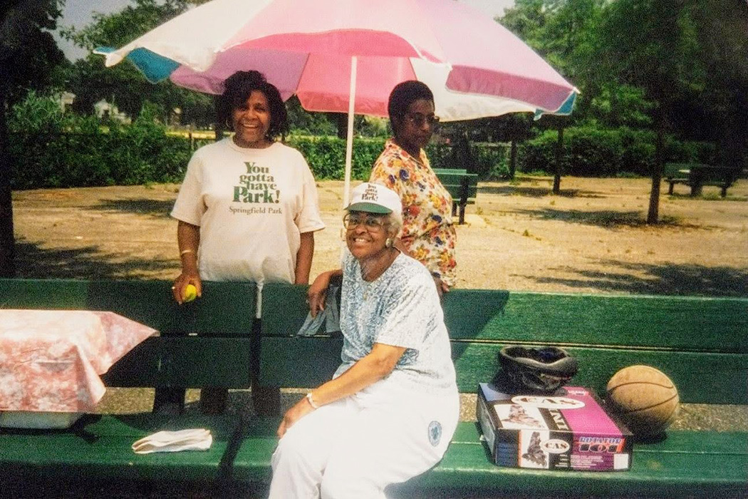 Community members enjoy the shade under the umbrella at the park benches