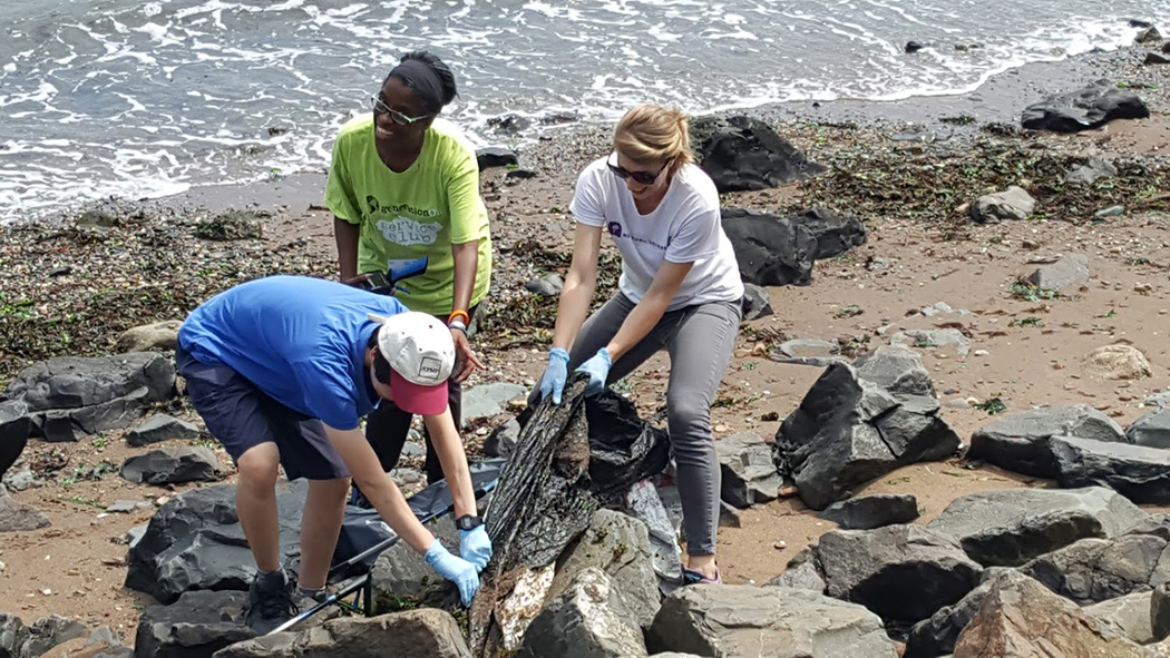 Community members pull out plastic from between the rocks at a beach