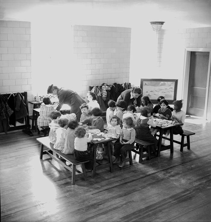 black and white archival image of kids seated together in an indoor playroom 