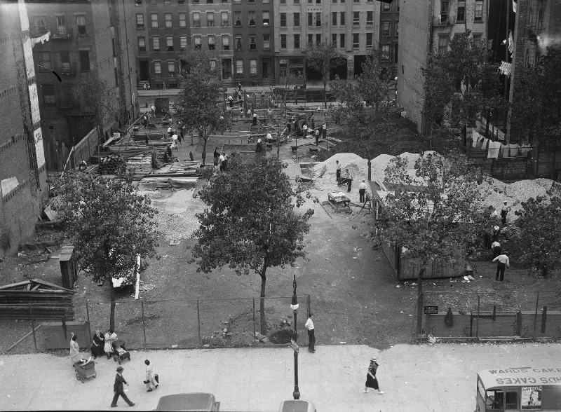 black and white archival image of a bird's eye view of community members stopping to look at the construction site as they pass by