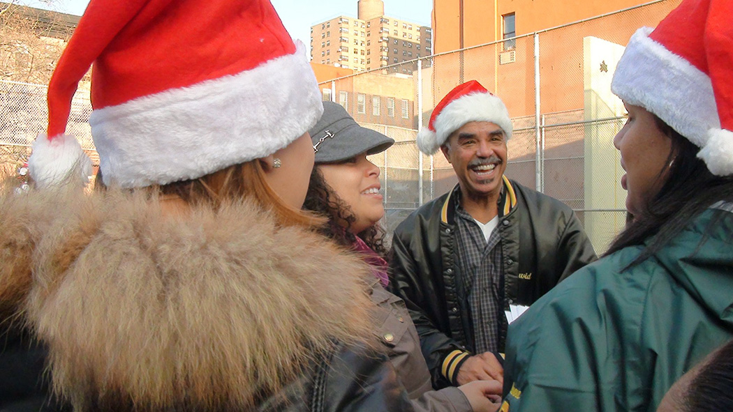 Community members wearing Santa hats share a laugh in the park