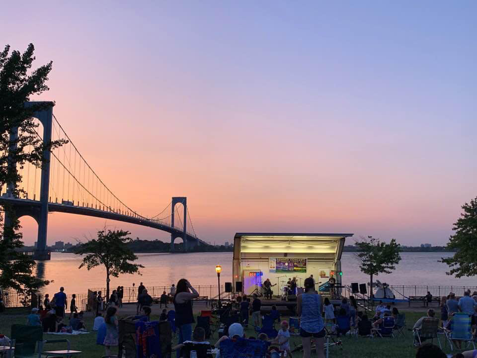 Neighbors settle in for a performance at the waterfront of the park which features a beautiful view of the Whitestone bridge at Sunset