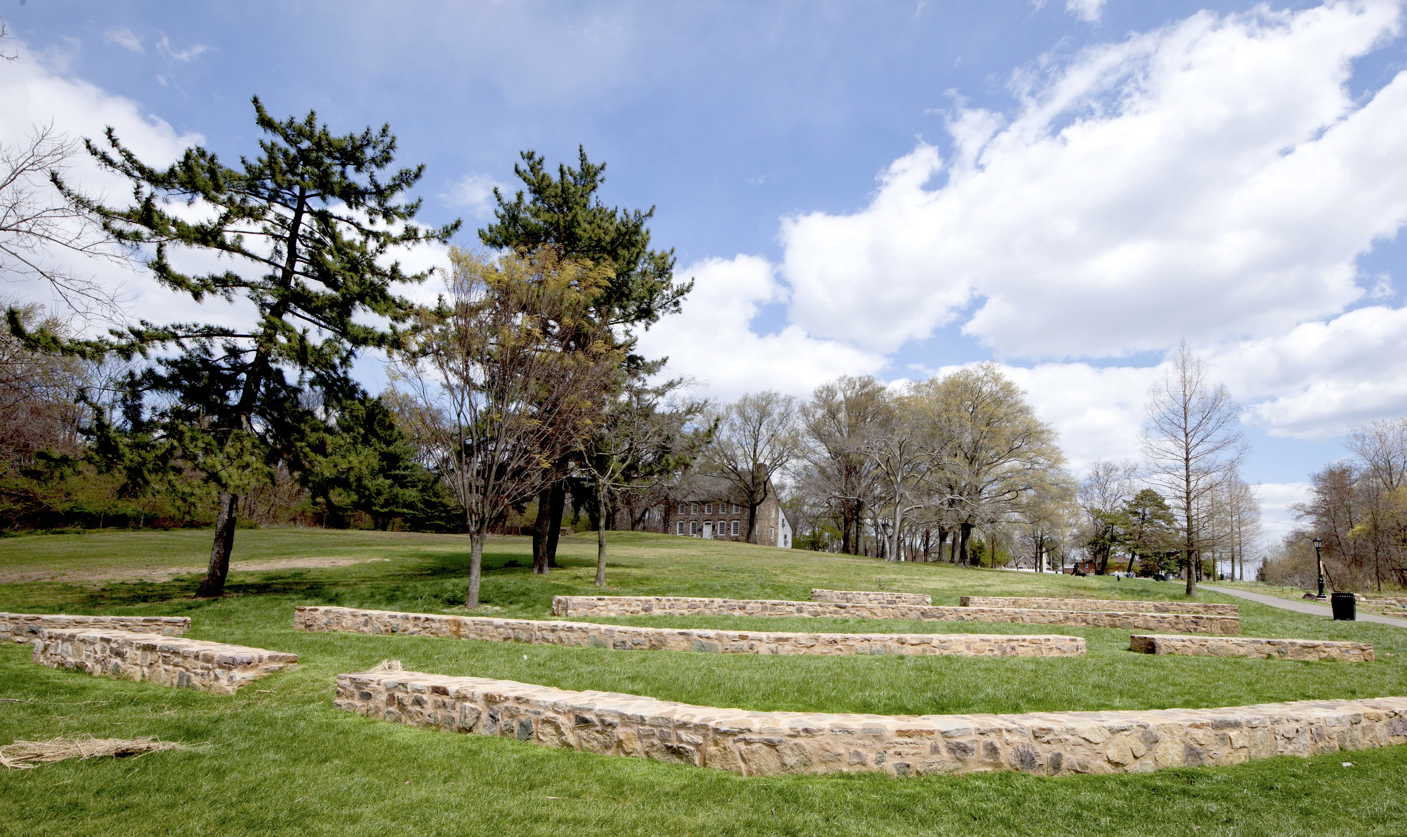 conifers tower over an amphitheater style seating area in front of an old historic house on the hill