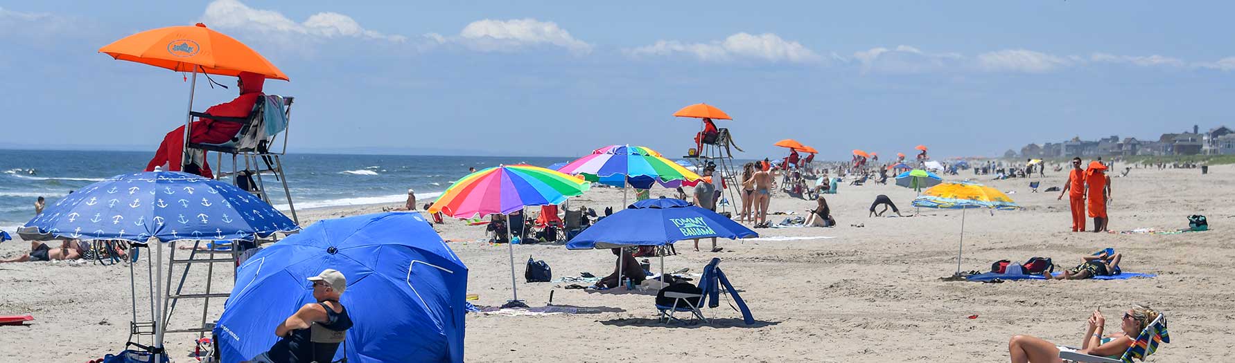 A view of the beach showing lifeguards at their stations looking out at the water as beachgoers relax on the sand