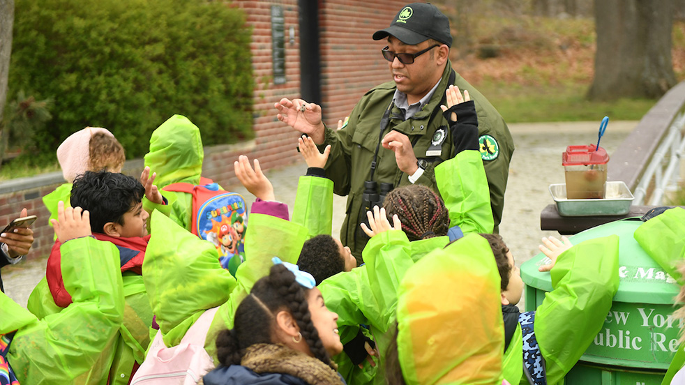 a park ranger takes questions from young students while holding up an insect