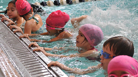 Kids hold on to the edge of the pool while learning how to swim