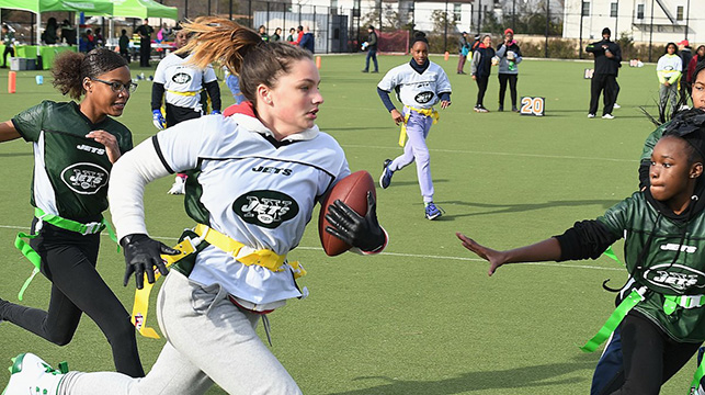 teens play flag football on a field in the park