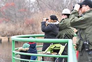 People in park ranger uniforms and families are looking out at nature over a clearing.