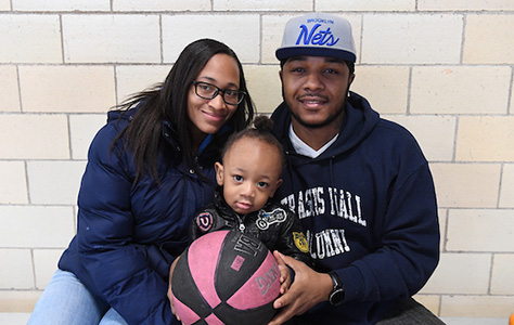 A father, mother, and toddler sit together holding a basketball