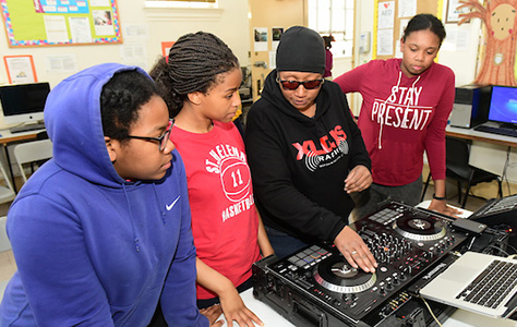 An instructor showing teens how to operate a digital turntable attached to a laptop computer