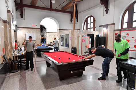 A group of people gather to play billiards in the hallway of a recreation center.