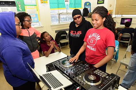 A group of students gather around DJ equipment as one works on their track.