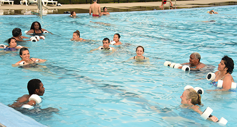 People in an outdoor pool holding workout equipment.