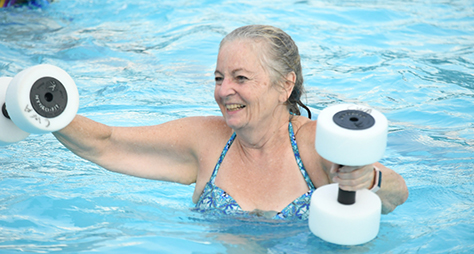 A senior swimmer holding weights in a water aerobics class.