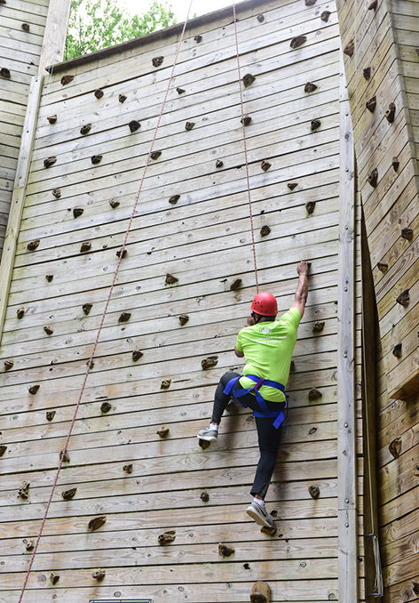 A person reaching for the next handhold on a climbing wall while wearing safety equipment.