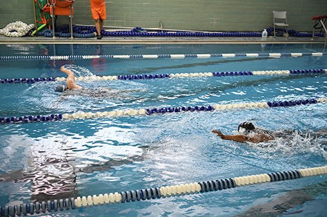 Three swimmers in separate lanes swimming laps at an indoor pool.