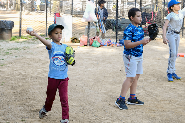 A young child enthusiastically throws a baseball, accompanied by other children in the middle of a sports clinic.