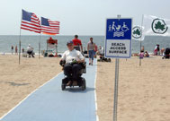 Man in wheelchair on beach mat next to sign reading Beach Access Path